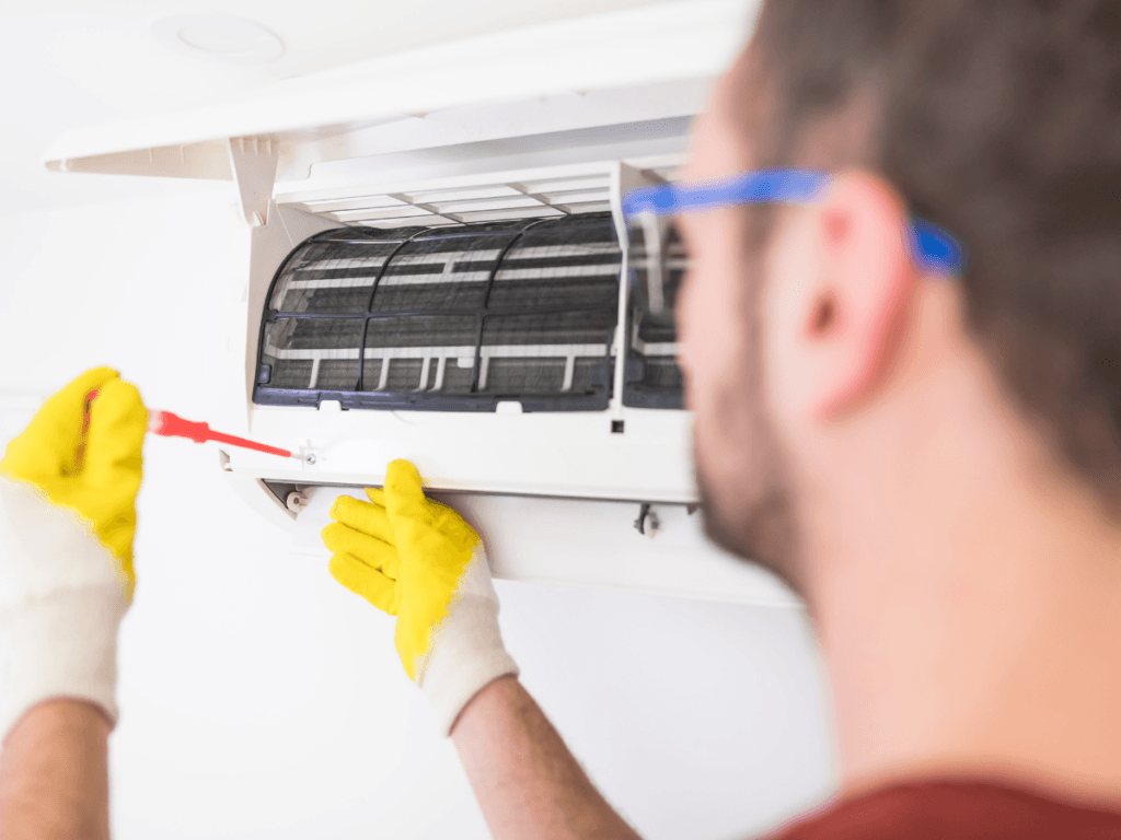 Person wearing gloves uses a screwdriver to repair or maintain a clean AC unit that is wall-mounted.