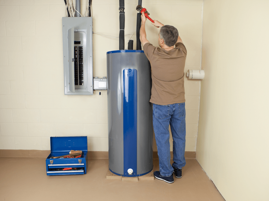 A man performs a traditional repair, using a pipe wrench to work on pipes above a water heater, with an electrical panel and a blue toolbox nearby.