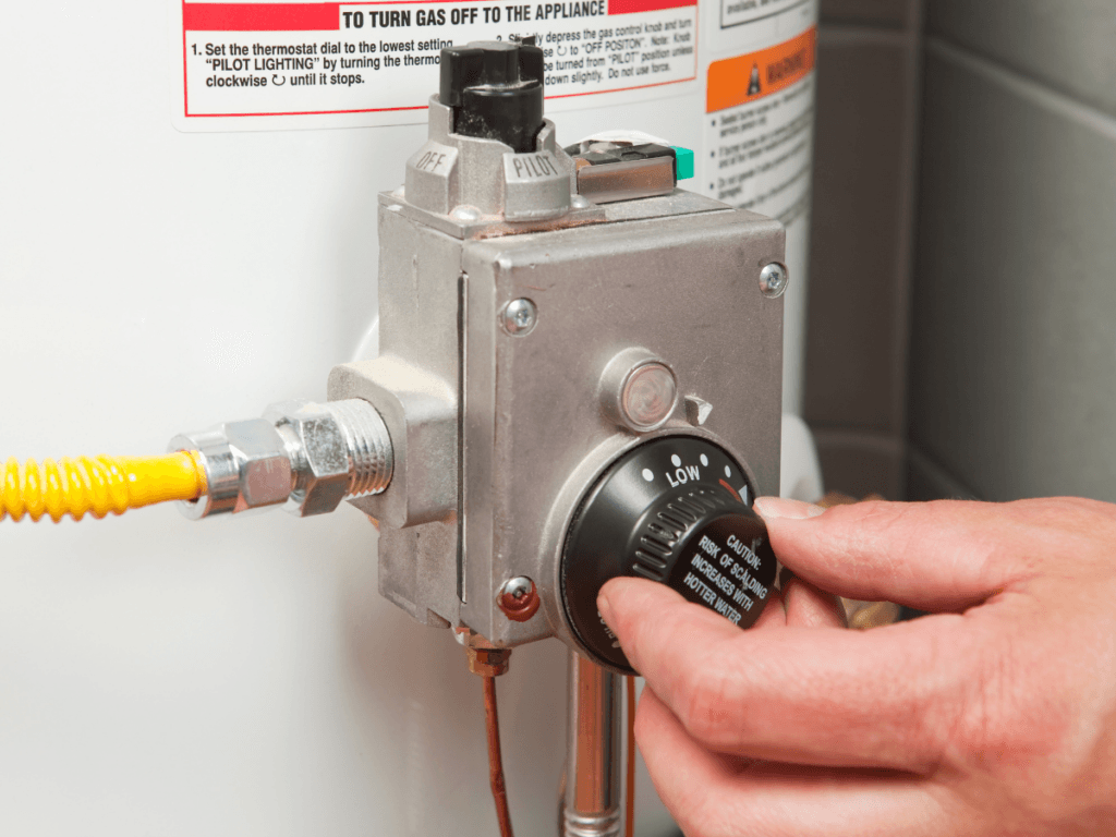 A person performs a traditional repair by adjusting the temperature dial on a water heater control valve, turning the knob from low to a higher setting.