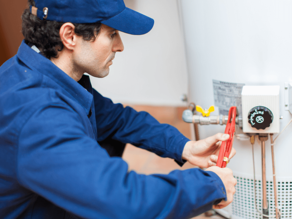 A technician in blue uniform uses a wrench to adjust a fitting on a water heater, demonstrating traditional repair techniques.