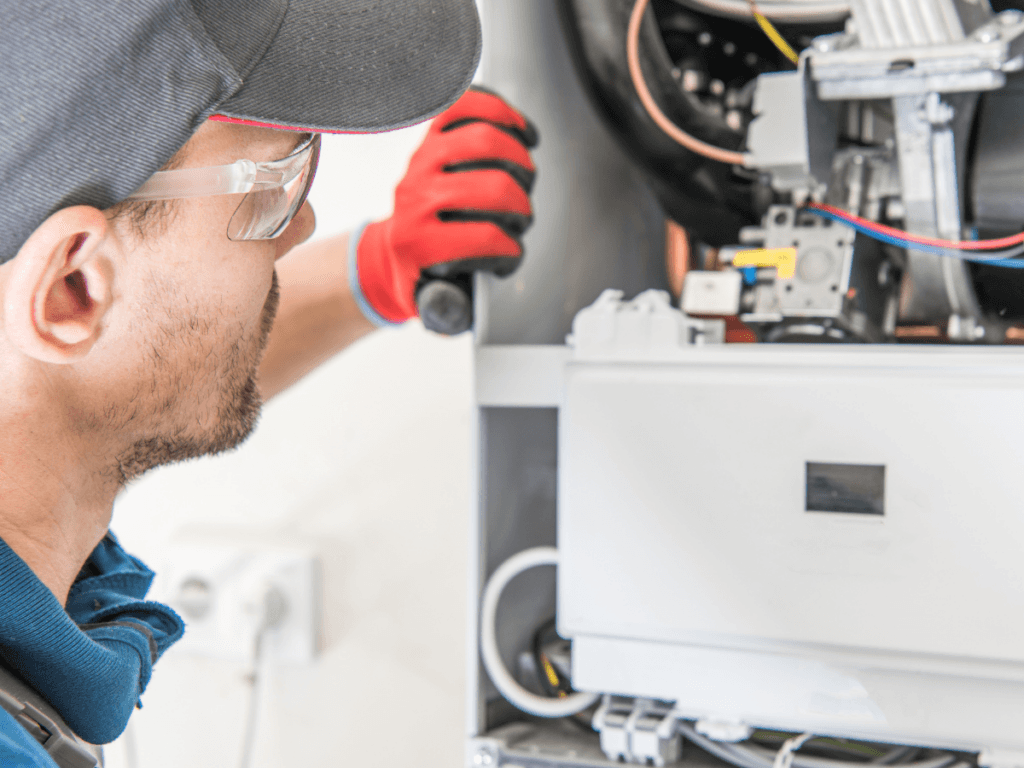 A technician wearing safety glasses and a red glove performs a traditional repair as they inspect or fix an open household appliance with exposed wiring and components.